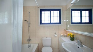 A bathroom with a bathtub, toilet, sink, and a window with blue frames. - Villa Julie in Protaras (Paralimni)