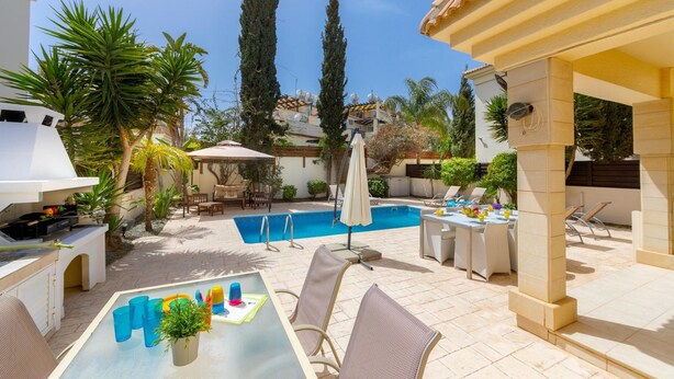 A poolside area with a barbecue, outdoor seating, and a view of the pool. - Protaras Villa Athamas Blue (Paralimni)