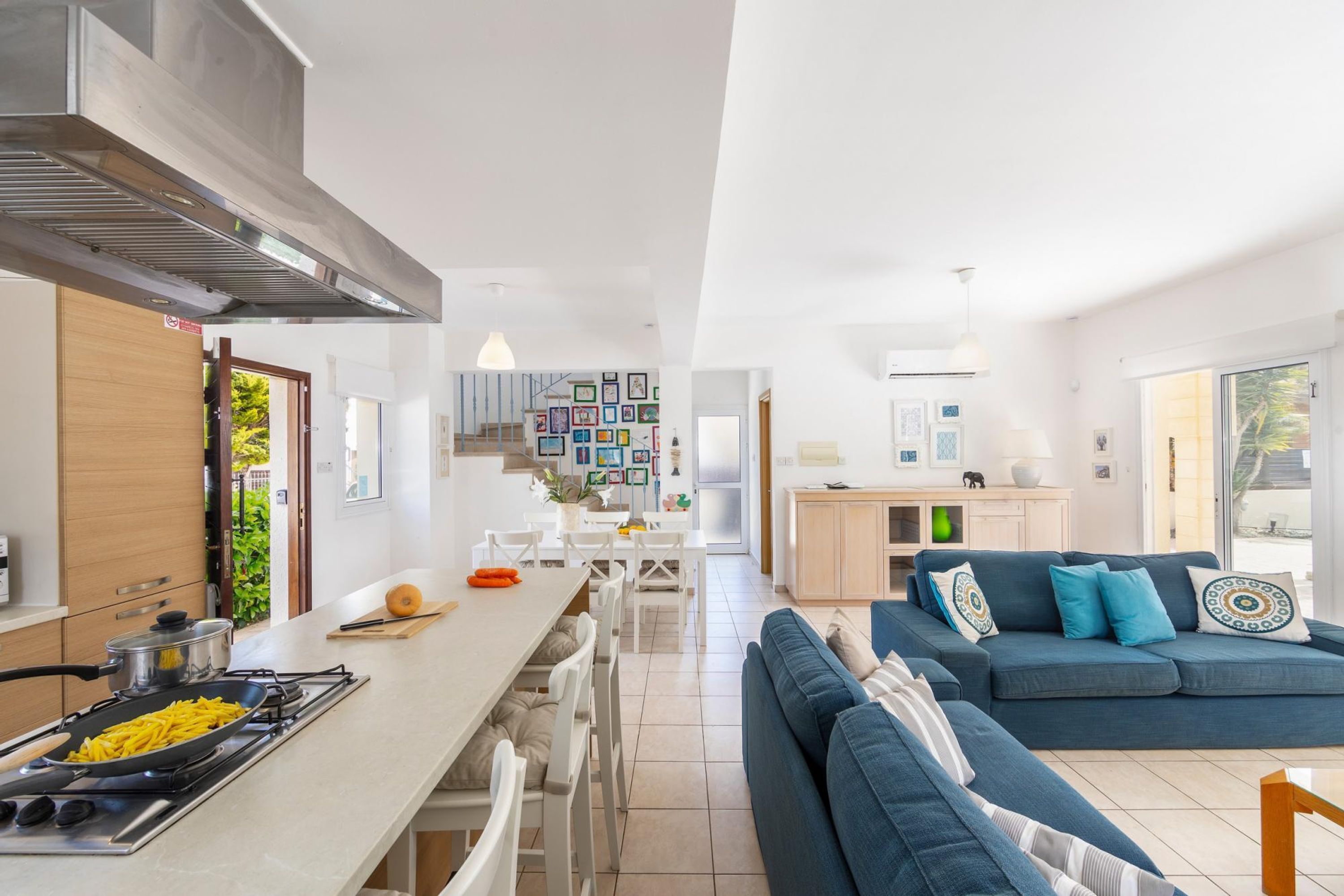 Cozinha moderna com fogão, mesa de jantar e cadeiras. Na área de estar, um sofá azul com almofadas decorativas.