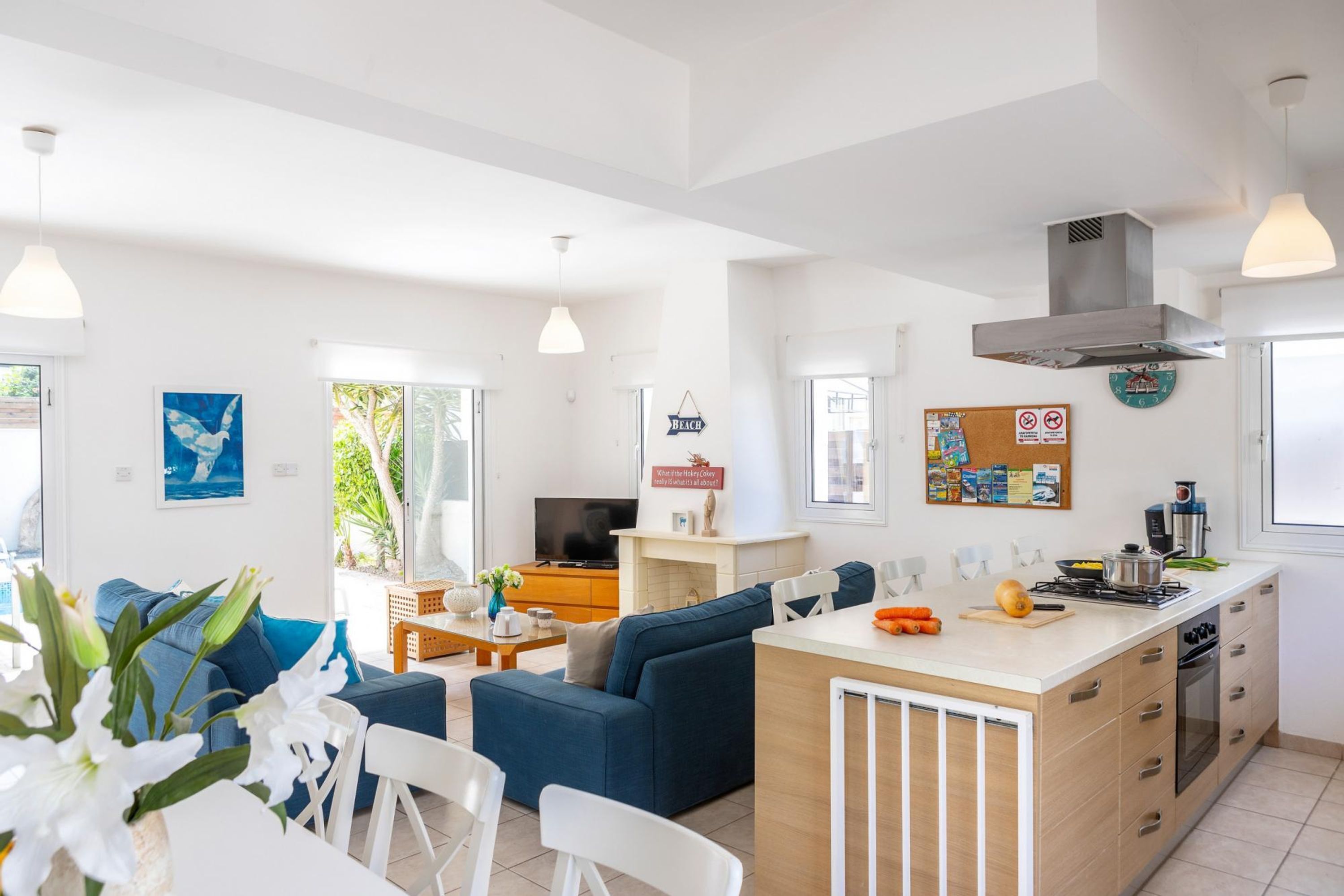 Una cocina moderna con una isla central, un área de comedor con un sofá azul y una sala de estar con televisor y obras de arte azules.