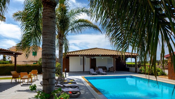 A swimming pool with lounge chairs, a covered seating area, and palm trees. - Cape Greco Palm Trees Villa (Ayia Napa)