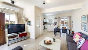 A modern living room with a flat-screen TV, a sofa, a coffee table, and a dining area with a table and chairs. - Cape Greco Palm Trees Villa (Ayia Napa)