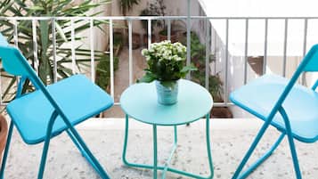 A balcony with two turquoise chairs and a small table, a potted plant, and a white railing.