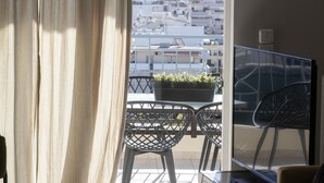 En balkon med et bord og stole, en potteplante og udsigt over bybilledet.