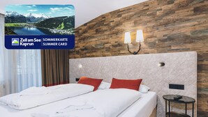 A hotel room with a large bed, two pillows, a nightstand, and a wall-mounted lamp. - Alpine City Living - TOP 32 (Zell am See)