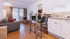A modern apartment with a living area, a dining table with chairs, a kitchen with white cabinets, and a large window with curtains. - Alpine City Living - TOP 32 (Zell am See)