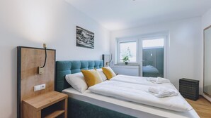 Un dormitorio moderno con una cama grande, una mesita de noche de madera, un televisor montado en la pared y una ventana con vistas al exterior.
