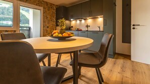 A modern kitchen with dark cabinets, a round dining table with chairs, and a fruit bowl on the table. - Tevini Alpine Apartments - Schmittenblick (Zell am See)