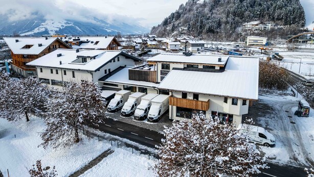 A snow-covered building with multiple parking spaces and a view of a mountainous landscape. - Tevini Alpine Apartments - Schmittenblick (Zell am See)