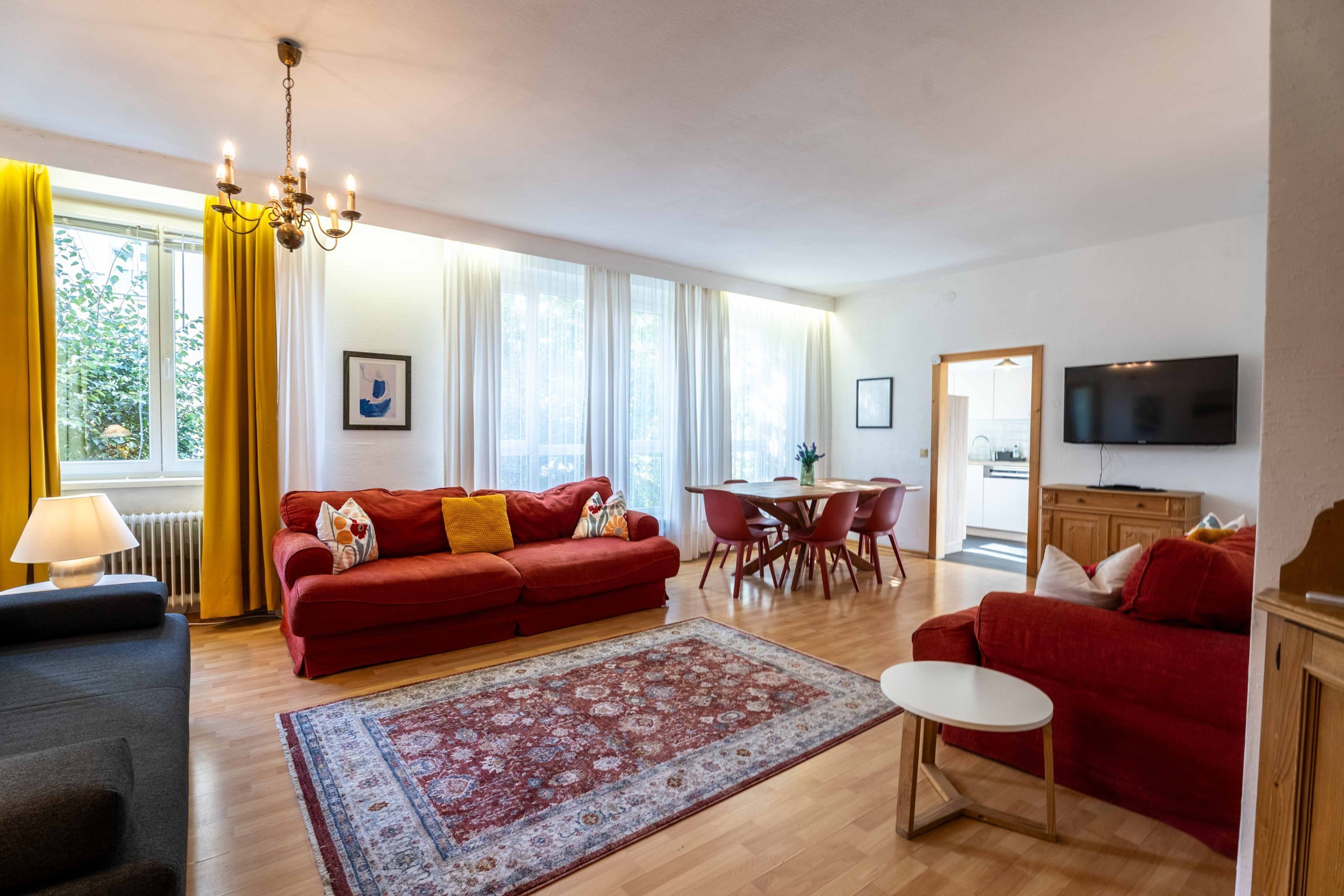 Een woonkamer met een rode bank, een eettafel en een televisie.