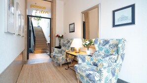 Un couloir avec un escalier, un canapé, une table avec une lampe et une enseigne indiquant « Pension Eden ».