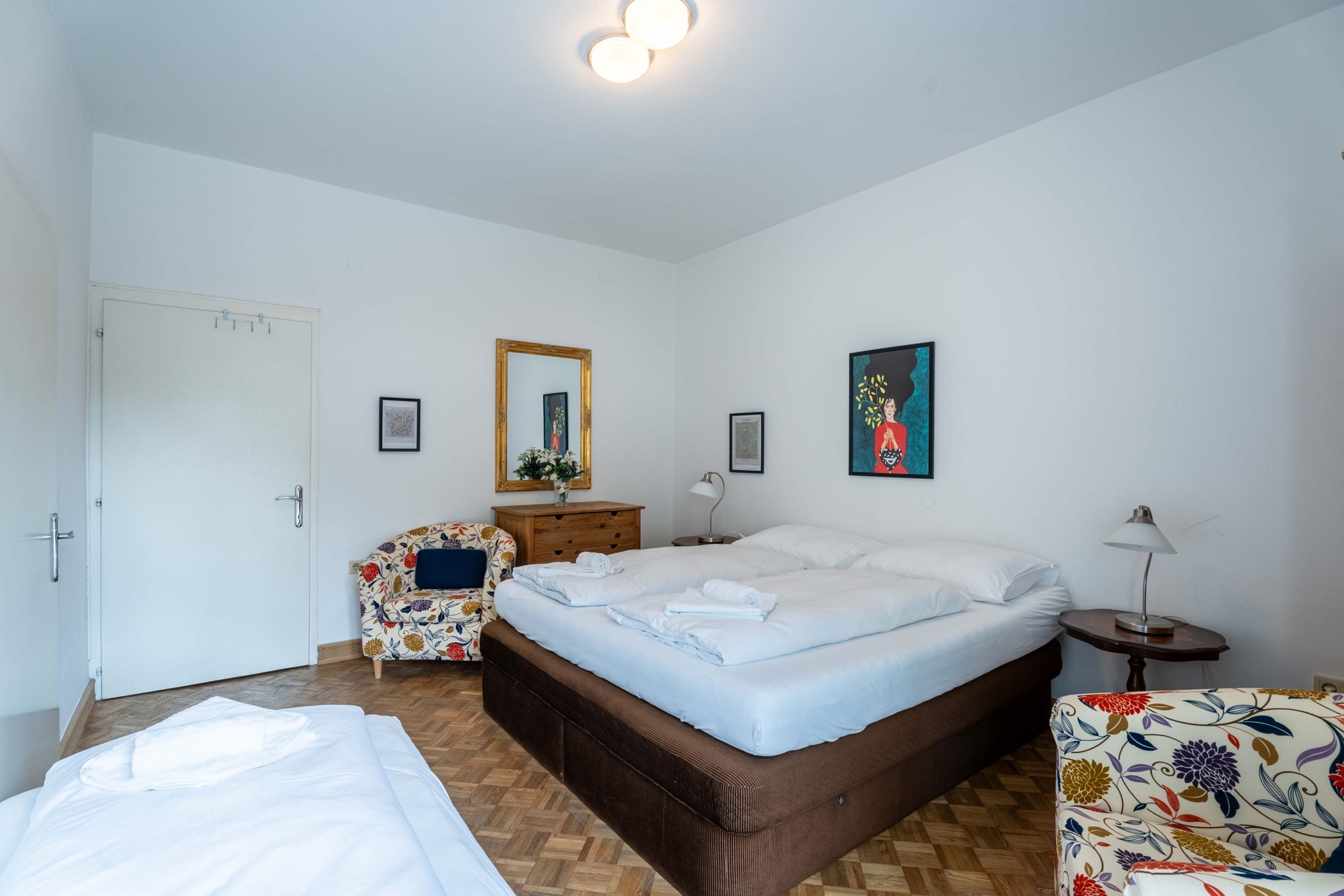 A bedroom with a bed, a chair, a dresser, a mirror, and a wall with a framed picture.