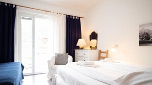 Une chambre d’hôtel avec un lit, une chaise, un bureau avec une lampe et une fenêtre avec des rideaux.