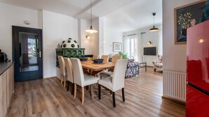 Un coin repas avec une table et des chaises en bois, un coin cuisine avec un réfrigérateur, et un salon avec un canapé et un fauteuil.