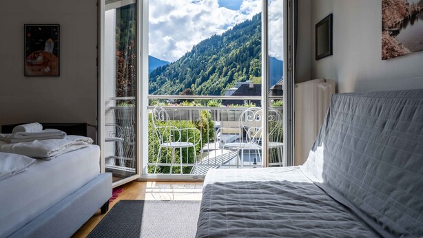 Une chambre à coucher avec un lit, une fenêtre et un balcon équipé de chaises et d’une table.