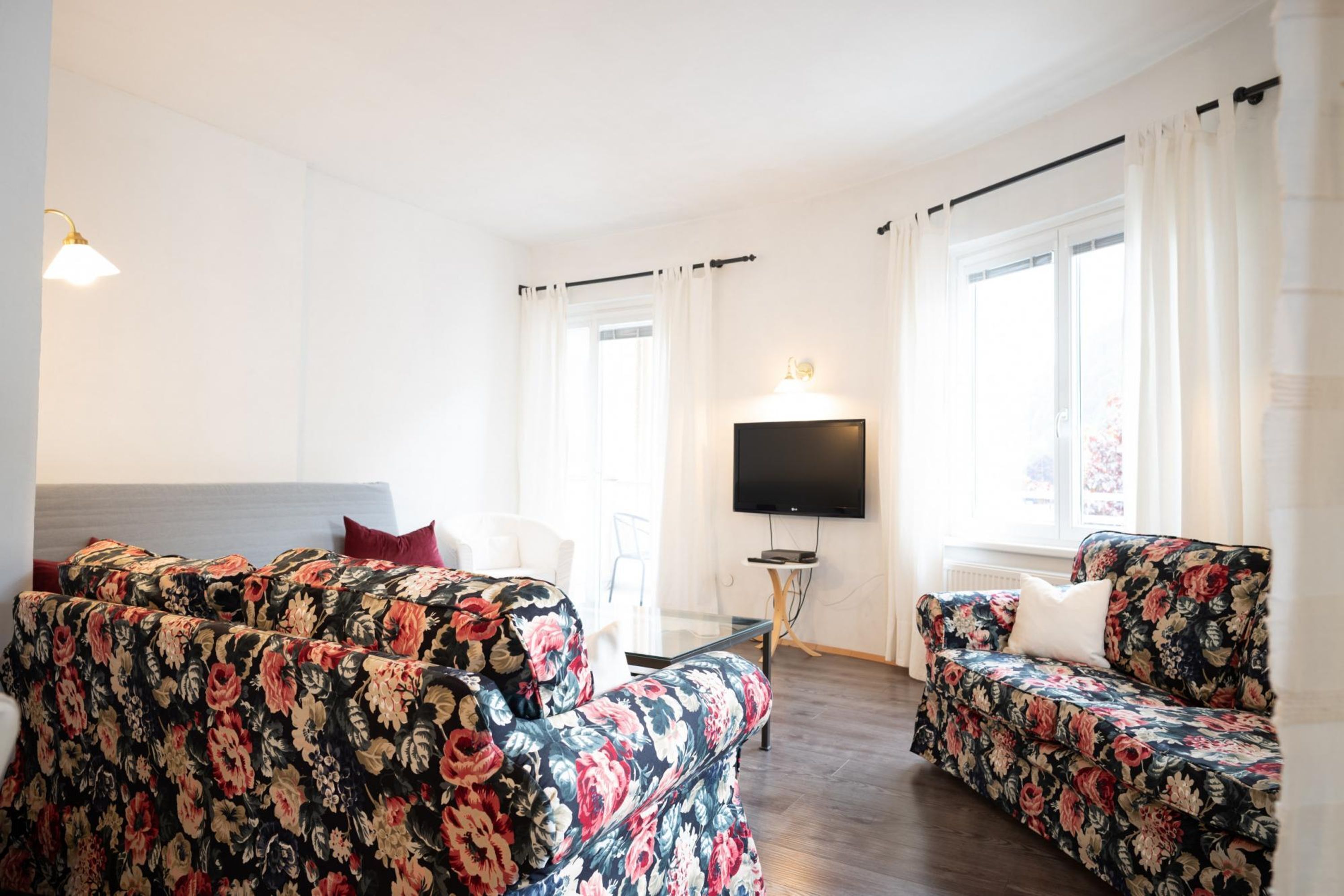 Quarto de hotel com uma cama grande, dois sofás com padrão floral, uma televisão de tela plana e uma mesinha.