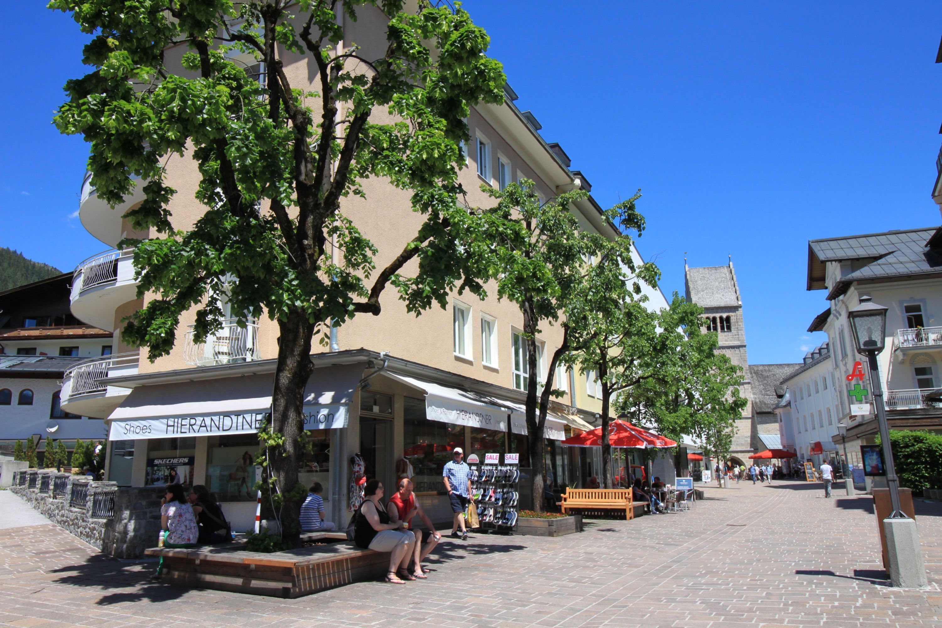 A pedestrian street with shops, benches, and trees.