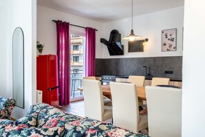A modern kitchen with a dining area, red cabinets, and a balcony with pink curtains. - Living Eden - TOP 14 (Zell am See)