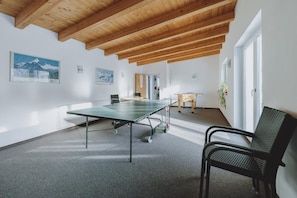 A room with a ping pong table, a chair, and a wooden ceiling.
