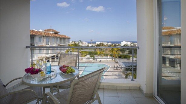A balcony with a table set for two, overlooking a swimming pool and a cityscape. - Poppy 209 in Protaras (Paralimni)