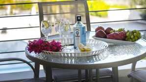 A table with a bottle of Bombay Sapphire Gin, glasses with lime slices, a bowl of grapes, and a plate of red fruits, set on a balcony with a view. - Poppy 209 in Protaras (Paralimni)
