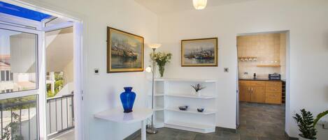 A modern interior with a white wall, a blue vase on a white table, and a kitchen area with wooden cabinets and a tiled backsplash.