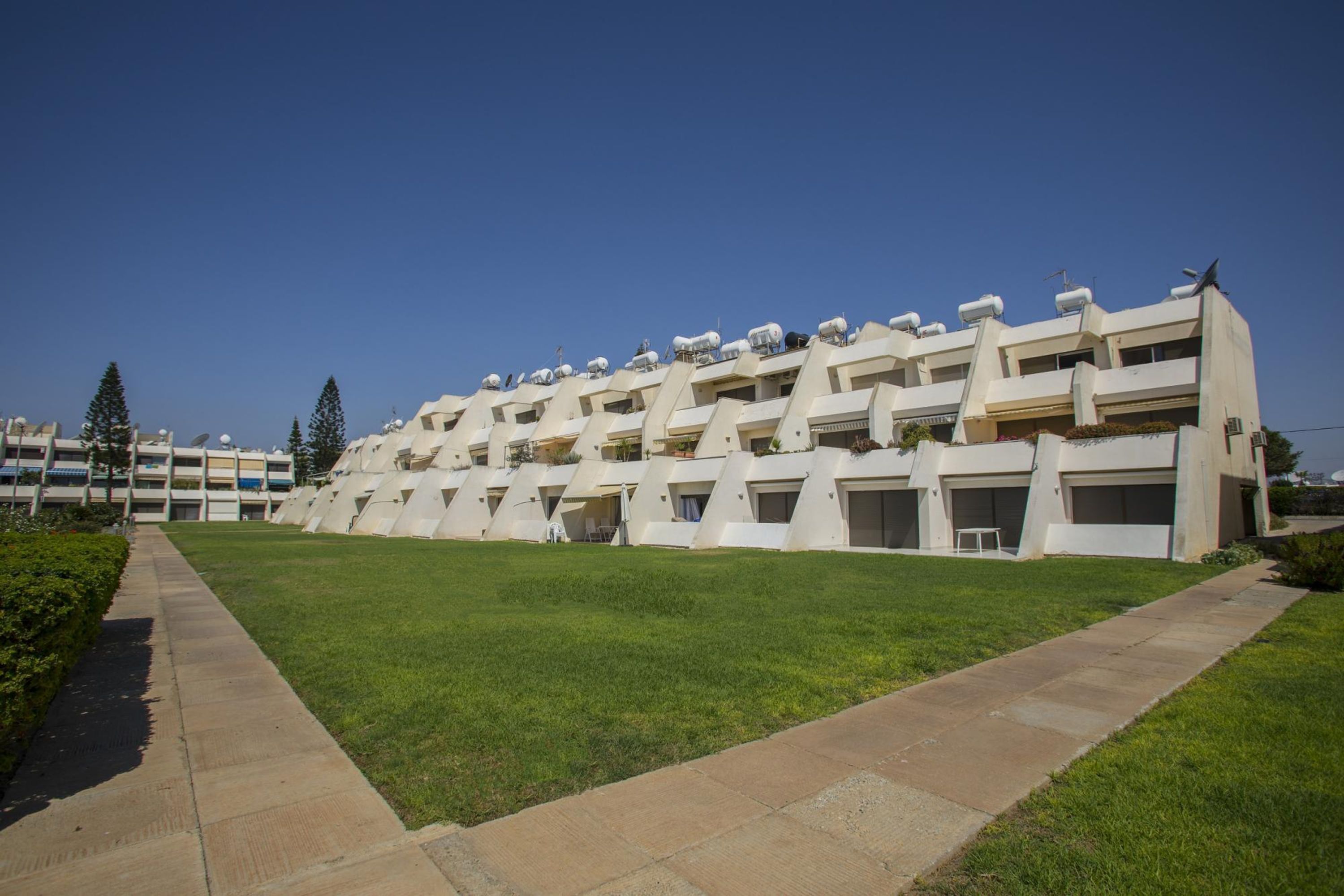 A modern multi-story building with a flat roof, multiple balconies, and a central courtyard.