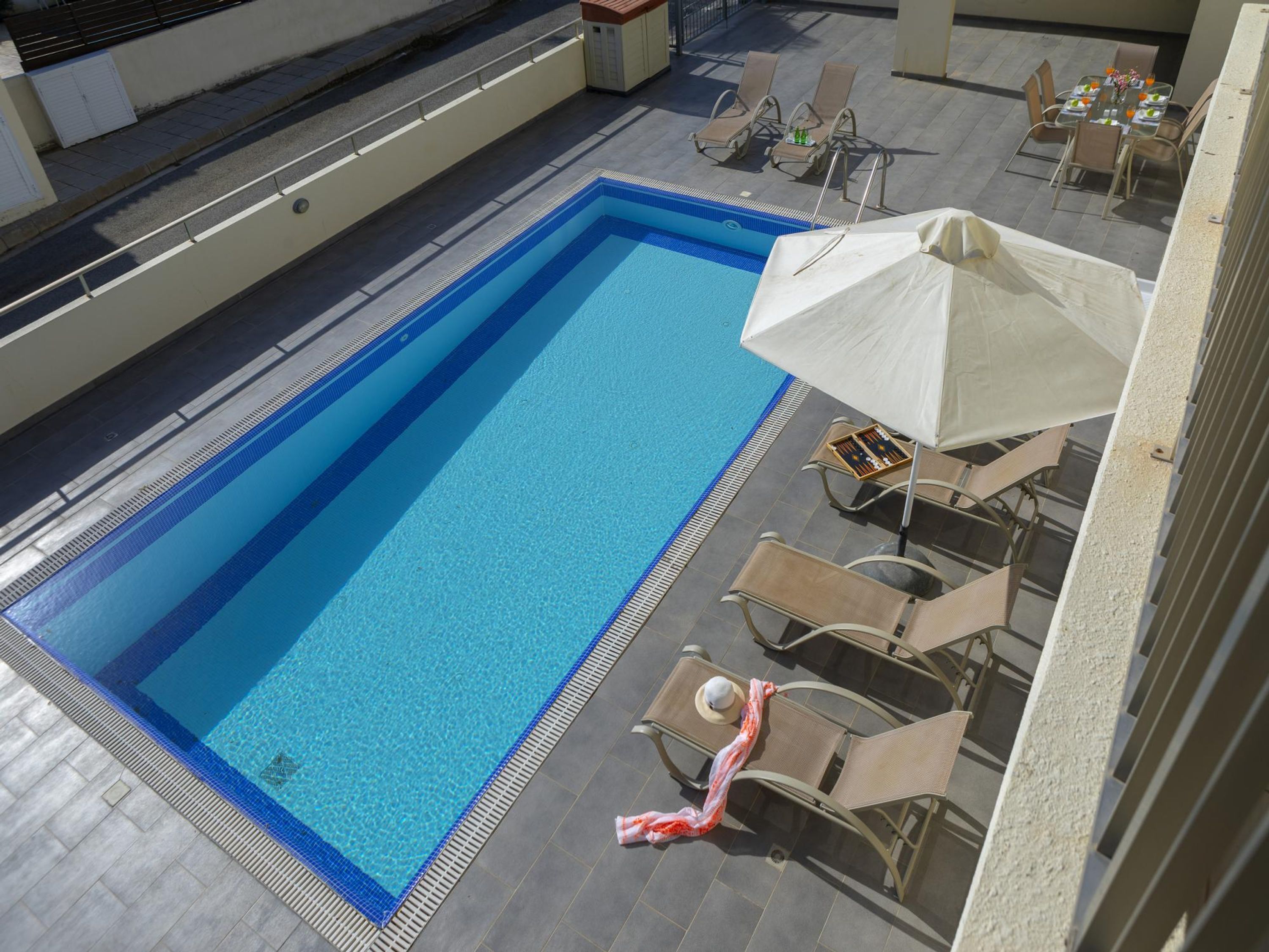 Una piscina rettangolare con bordi piastrellati, circondata da lettini e un tavolo ombrellato.