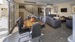 A modern living room with a dining area, grey sofas, a wooden dining table, and a staircase leading to an upper level. - Theodora 1 in Protaras (Paralimni)