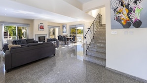 A spacious living area with a dark grey sofa, a fireplace, and a staircase leading to an upper level. - Theodora 1 in Protaras (Paralimni)