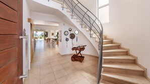 A spacious interior with a wooden staircase, a dining area, and a wall decorated with clocks and wall hangings. - Protaras Beachfront Villa Pietra (Paralimni)