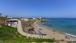 A coastal beach with a paved walkway, beach umbrellas, and a few people. - Protaras Beachfront Villa Pietra (Paralimni)