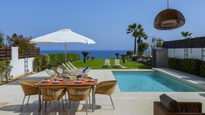A poolside dining area with a table set for four, overlooking a swimming pool and the sea. - Protaras Beachfront Villa Pietra (Paralimni)