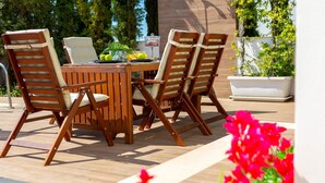 Een houten eethoekset buiten, bestaande uit vier stoelen en een tafel, omgeven door potten met planten en bloemen.