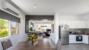 Een moderne keuken met witte kastjes, roestvrijstalen apparatuur en een eethoek met een houten tafel en stoelen.