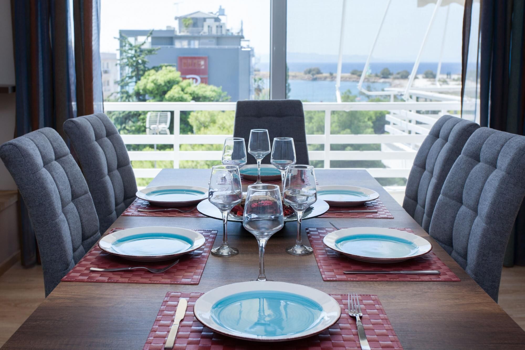 A dining table set for six with plates, glasses, and cutlery, overlooking a scenic view.