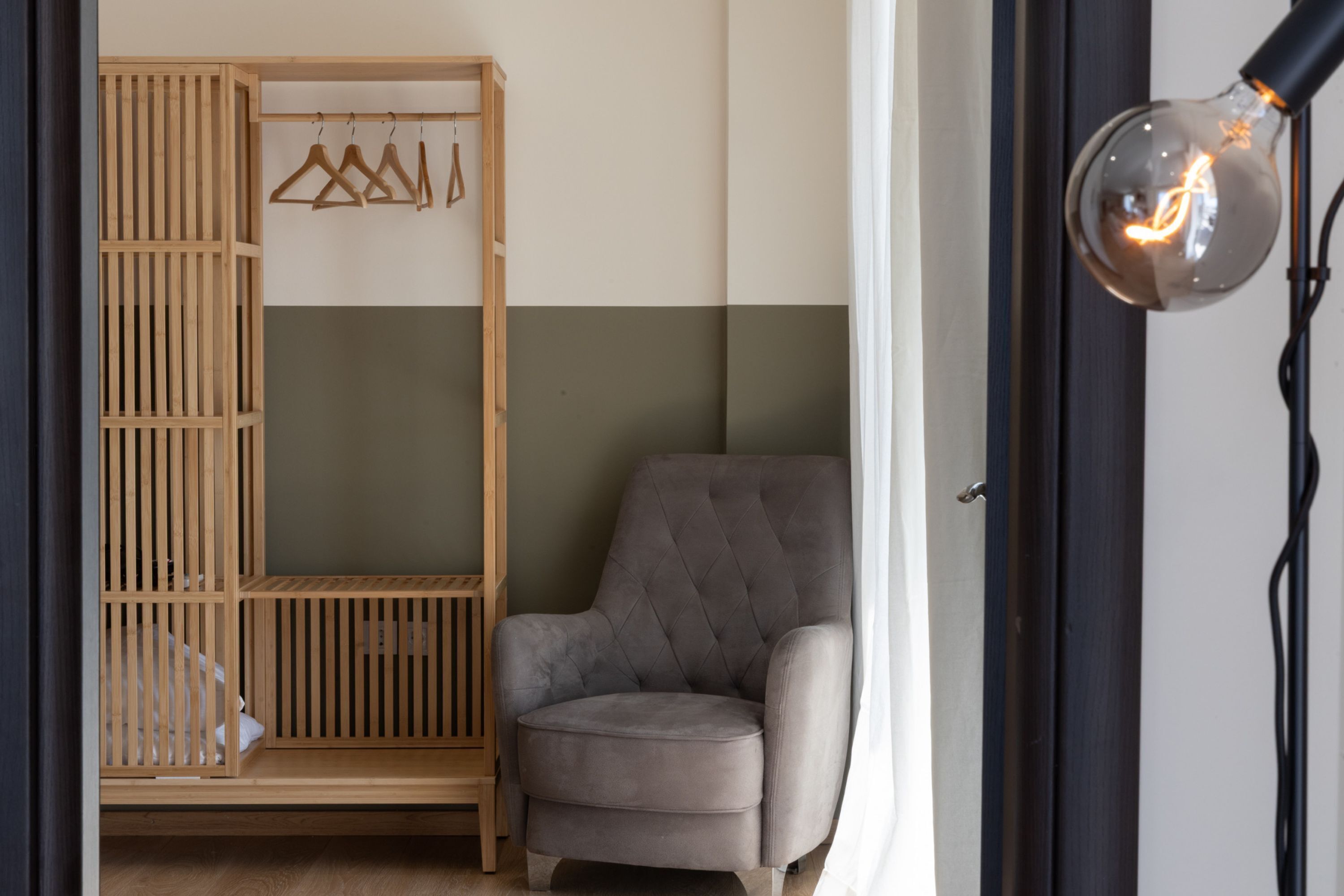 A room with a grey armchair, a wooden wardrobe, and a hanging light fixture.