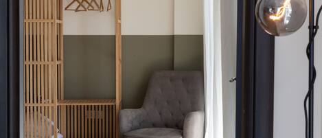 A room with a grey armchair, a wooden wardrobe, and a hanging light fixture.