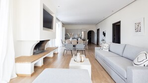 Una sala de estar moderna con chimenea, un sofá gris y un comedor al fondo.
