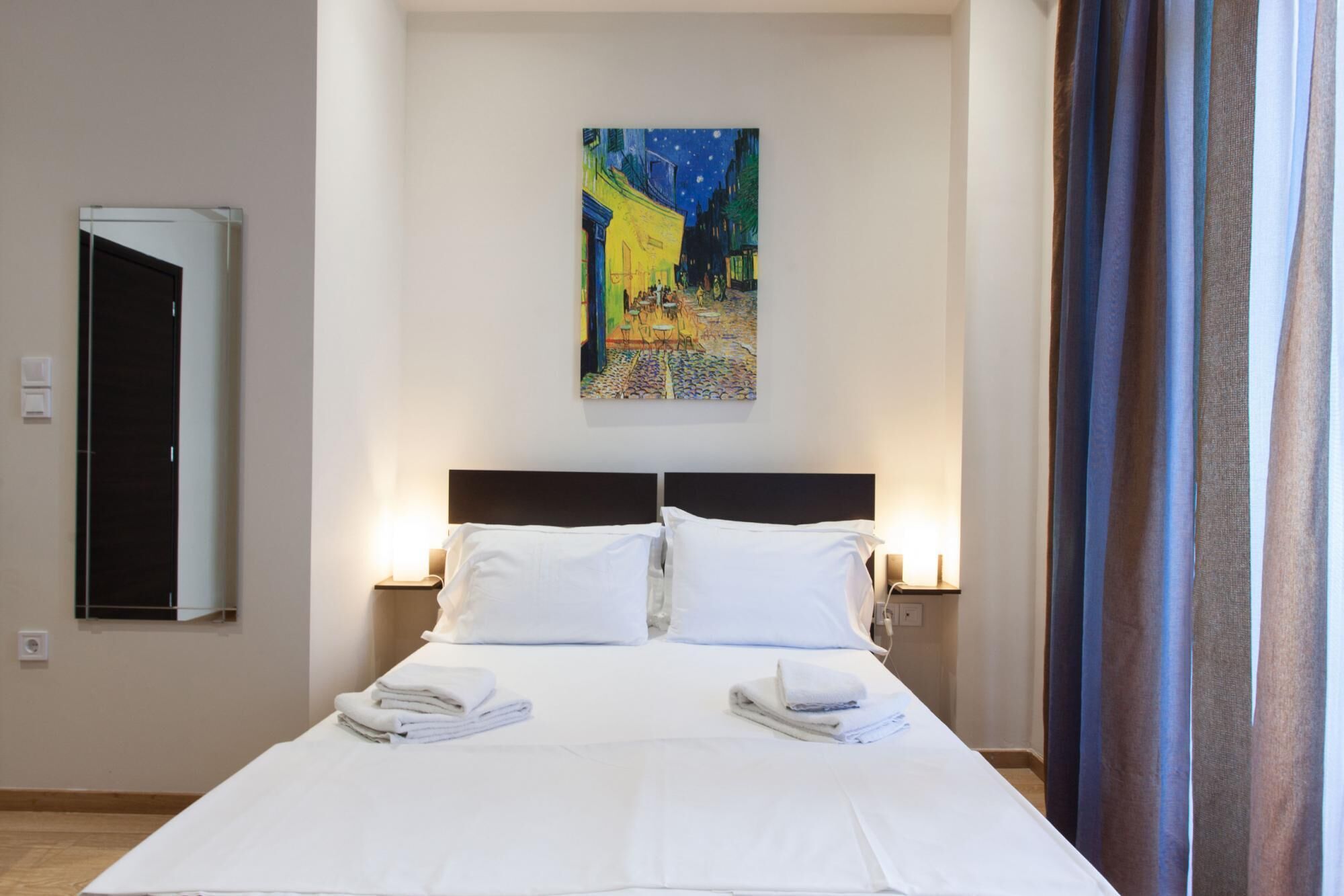 Una habitación de hotel con cama, un cuadro en la pared y una ventana con cortinas.