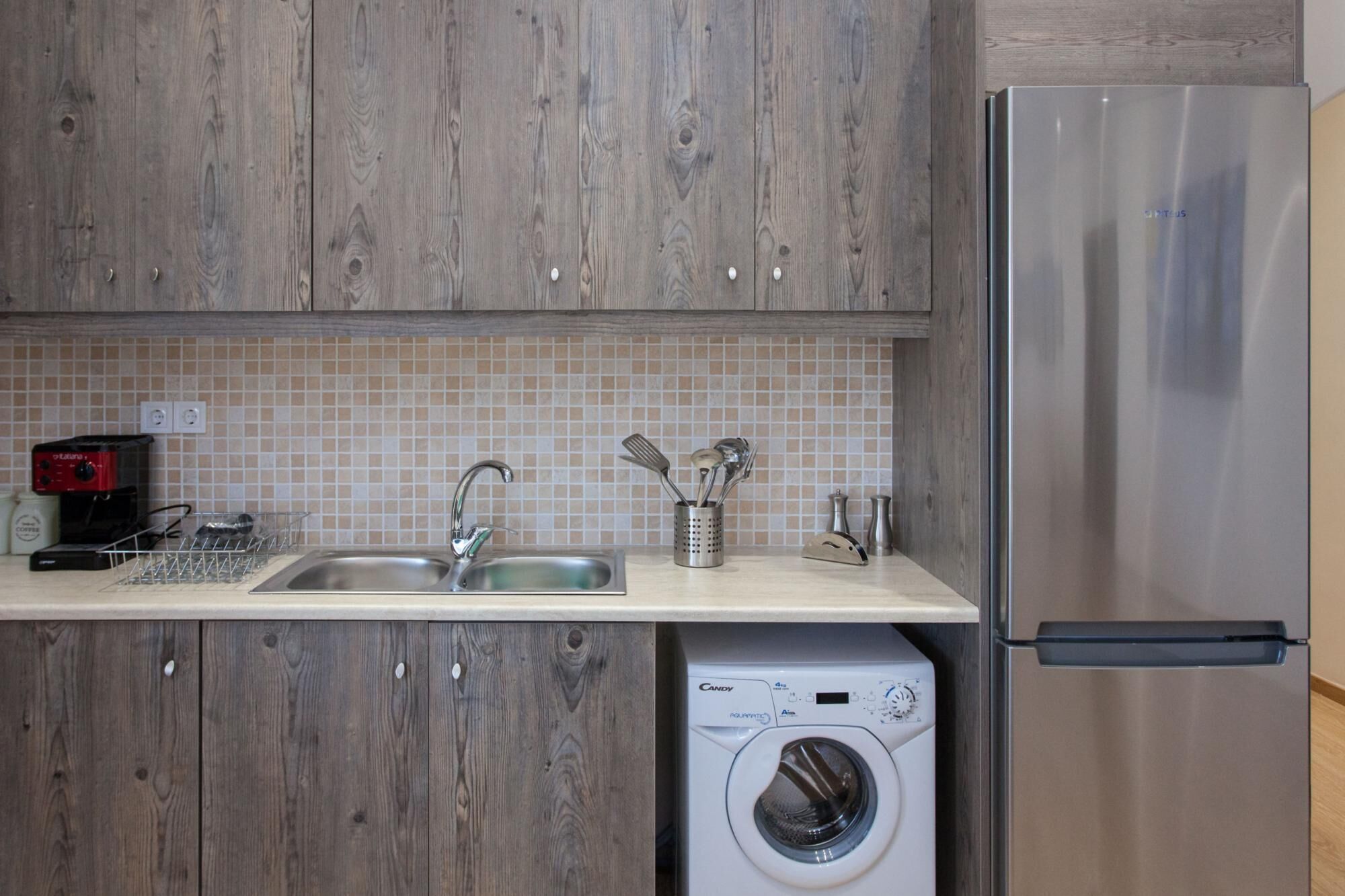 A kitchen with wooden cabinets, a stainless steel refrigerator, a washing machine, and a coffee maker.