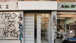 A storefront with a closed metal door, a scooter parked outside, and graffiti on the wall. - Explore Nightlife Near an Apartment With an Acropolis View (Athens)