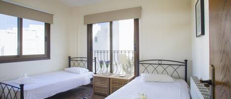 A bedroom with two single beds, a window with a view, a wooden stool, and a radiator.