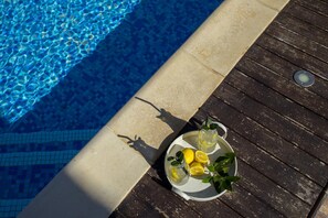 Une terrasse en bois au bord d’une piscine, avec un plateau contenant des citrons, des verres et une plante.