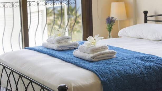A neatly made bed with a blue quilt, white pillows, and two folded white towels with white flowers on top. - Villa Buena Vista in Protaras (Paralimni)