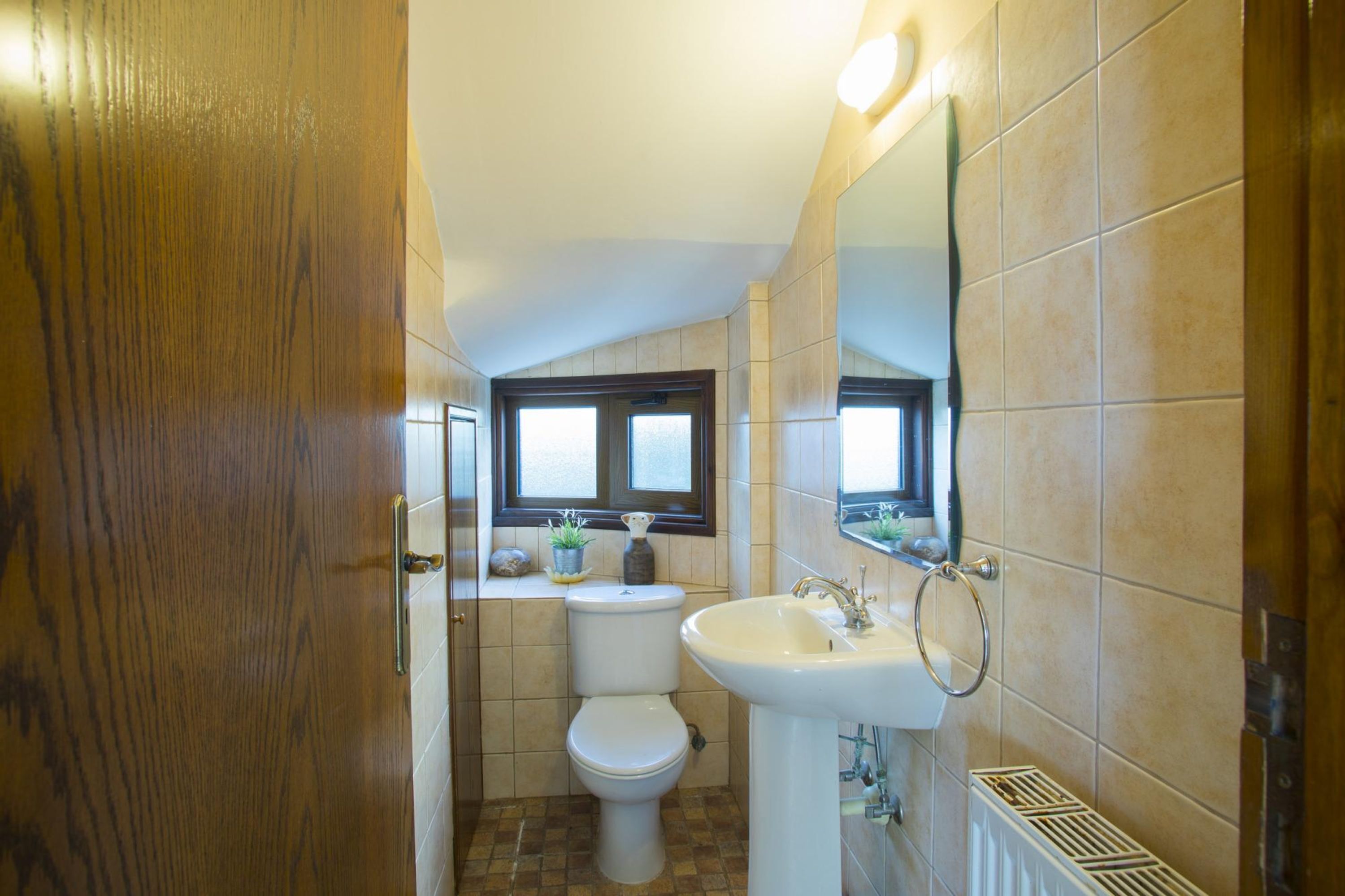A bathroom with a wooden door, a toilet, a sink, and a window above the toilet.
