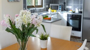 A modern kitchen with white cabinets, a microwave, and a refrigerator. There is a dining table with a vase of flowers and a potted plant. - Villa Buena Vista in Protaras (Paralimni)