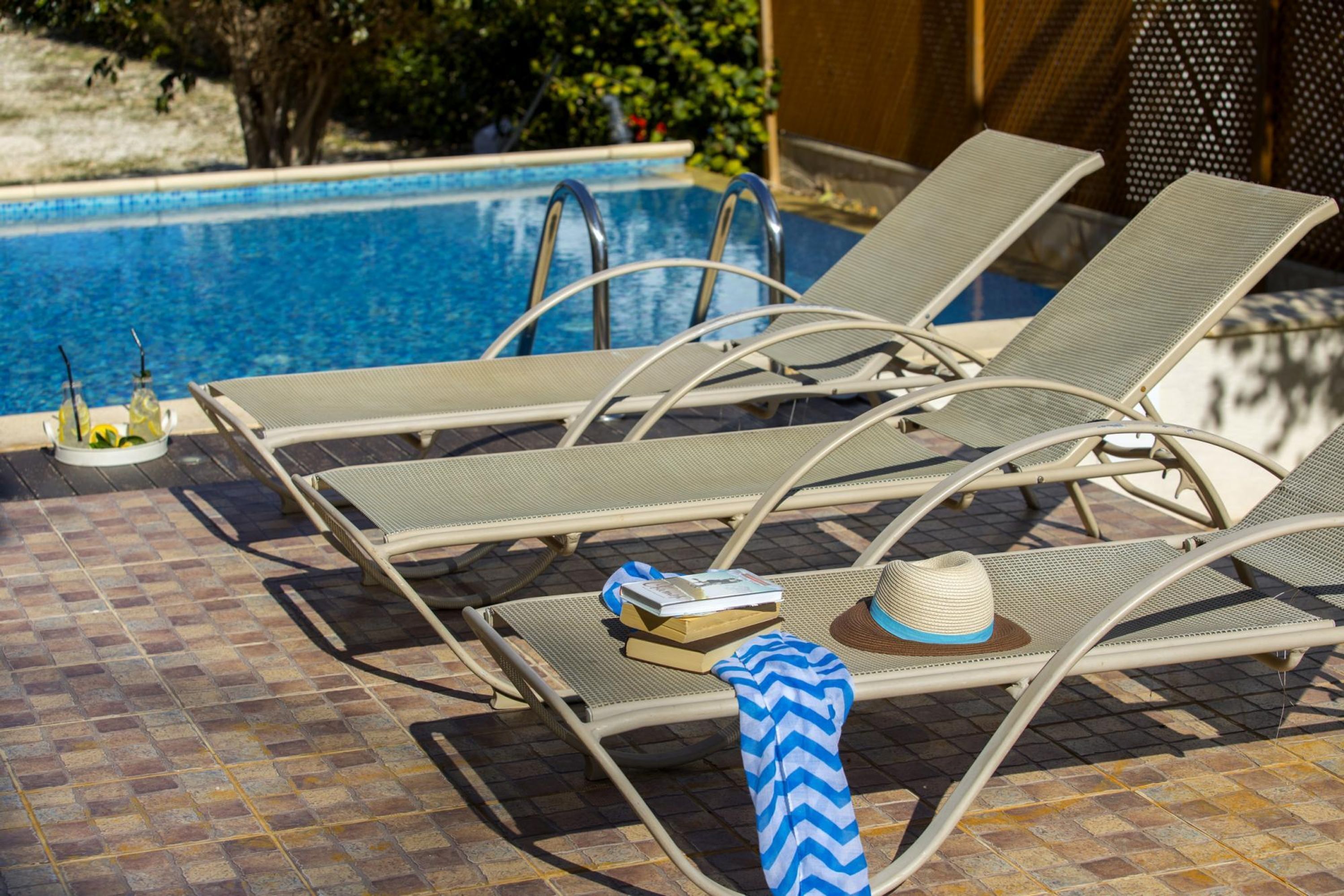 A poolside area with lounge chairs, a hat, and a book on one of the chairs.