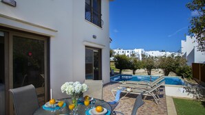 An outdoor dining area with a table set for two, a pool, and a view of the neighborhood. - Villa Buena Vista in Protaras (Paralimni)