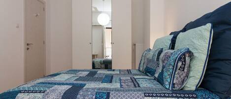 A bedroom with a large bed, a mirror, and a door leading to another room.